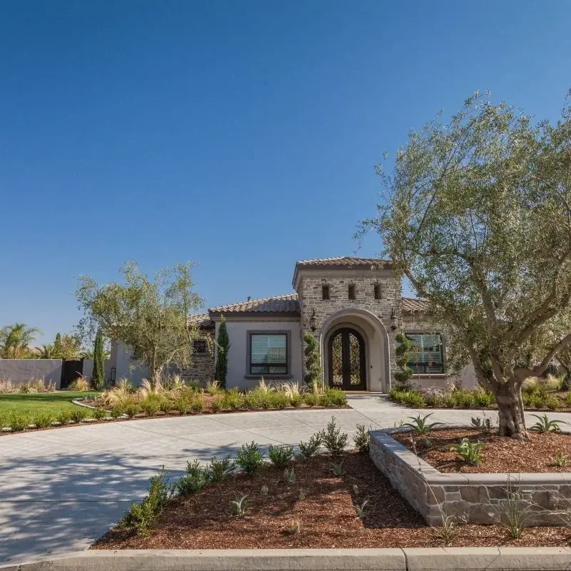 A circular driveway with a stone-faced planter island of agave, ornamental grasses and low-water shrubs in front of a stucco and stone home